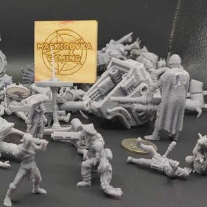 May include: A collection of gray miniature figurines, including soldiers, a tank, and various creatures. A wooden sign with the text "MASKIROVKA GAMING" is also present. The figurines are arranged on a dark surface.