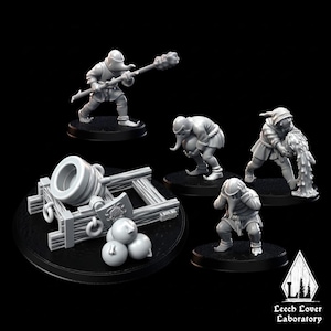 May include: A collection of miniature figurines and a cannon. The figurines depict medieval characters in various poses, including one holding a mace and another pouring a substance. The cannon is gray and sits on a wooden frame, with three cannonballs in front.