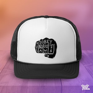 May include: Black and white trucker hat with a black fist graphic and the text "DISOBEY UNJUST LAWS".