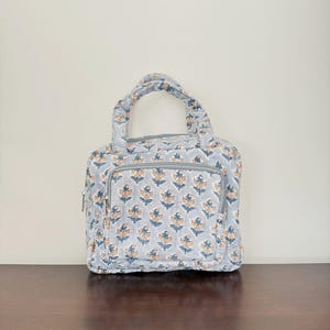 Peut inclure: Un petit sac fourre-tout gris avec un motif floral dans les tons bleus et orange. Le sac a deux poignées supérieures et une fermeture à glissière.