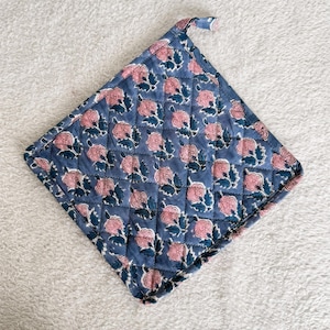 Può includere: Un presina trapuntata blu con un motivo floreale ripetuto rosa e blu scuro. La presina quadrata ha un anello per appenderla.