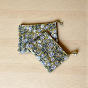 May include: Two quilted pouches with a floral pattern in olive green, white, and navy blue. The larger pouch is rectangular, and the smaller one is square. Both have a zipper closure and a small loop with a bead.