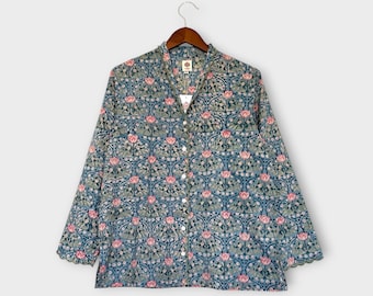 Op de afbeelding: Een overhemd met lange mouwen en een bloemenpatroon in blauw, groen en roze tinten. Het overhemd hangt aan een houten hanger. Het bloemmotief is ingewikkeld en bedekt het hele overhemd. Het overhemd heeft een kraag.