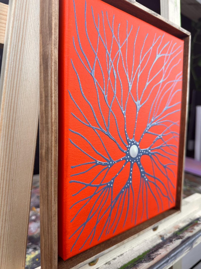 May include: A framed canvas painting with a bright orange background and a silver-grey tree-like design. The tree has a white circle in the center.