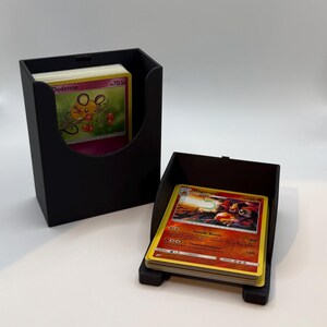 Può includere: Due porta carte neri, uno verticale e uno angolato, ciascuno pieno di carte collezionabili colorate. Le carte presentano vari personaggi e disegni. I porta carte sono realizzati in materiale nero opaco.