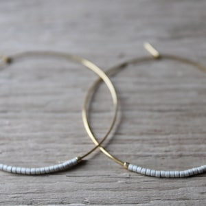 May include: A pair of gold hoop earrings with a row of small white beads on each hoop.