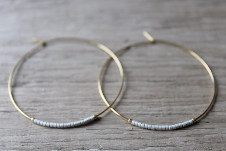 May include: A pair of gold hoop earrings with a row of small white beads on each hoop.