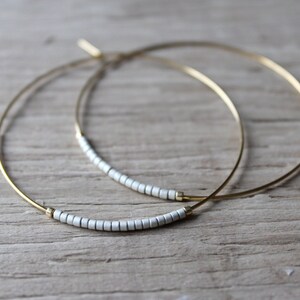 May include: A pair of gold hoop earrings with a row of white beads on each hoop.