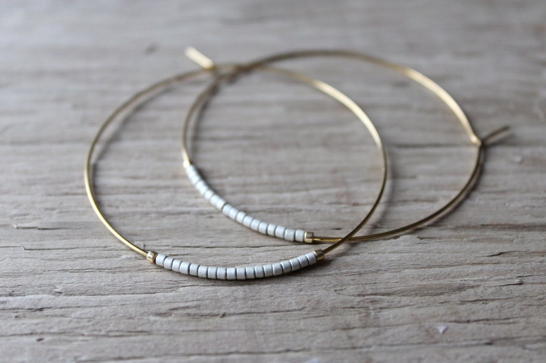 May include: A pair of gold hoop earrings with a row of white beads on each hoop.