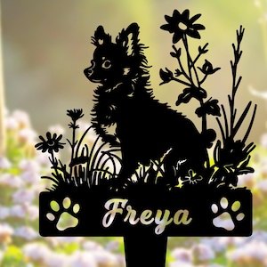 K&ouml;nnte beinhalten: Schwarze Metallsilhouette eines kleinen Hundes, der in einem Blumenfeld sitzt, mit dem Namen "Freya" auf einer darunter liegenden Plakette.
