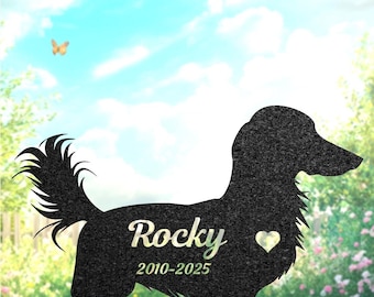 May include: A black metal dachshund silhouette with the name "Rocky" and dates 2010-2025, with a heart detail. The background features a blue sky, a butterfly, and a garden setting. The text "H. L. L. y a G I F. T" is at the top.