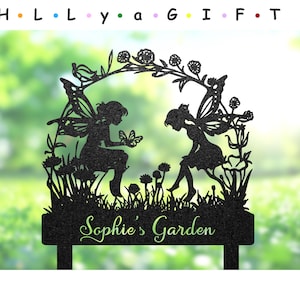 May include: Black metal garden stake featuring two fairy silhouettes within a floral arch. One fairy holds a butterfly, the other admires flowers. The stake reads "Sophie's Garden" in green script, with the word "GIFT" at the top.