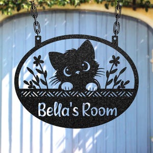 May include: Black metal sign with a cut-out design featuring a cat peeking over a decorative border. The sign is oval-shaped and includes the text "Bella's Room" in a cursive font. It hangs from chains.