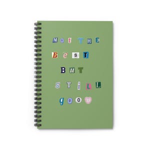 Könnte beinhalten: Ein salbeigrünes Notizbuch mit Spiralbindung und dem Text "Not the best but still good" auf dem Einband. Die Buchstaben sind im Stil eines Erpresserbriefs mit verschiedenen Schriftarten, Farben und Größen gestaltet, und das Wort "good" endet mit einem rosa Herz.