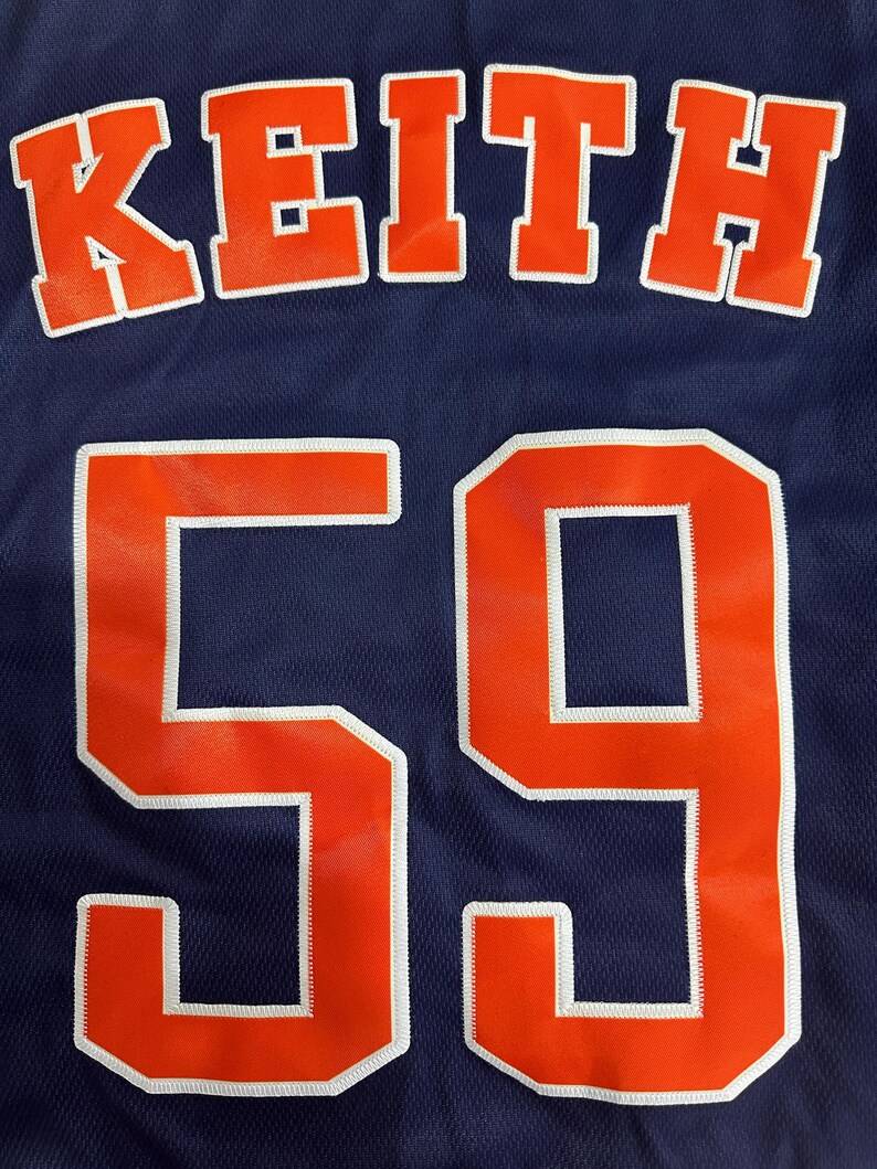 May include: A navy blue jersey with the name "KEITH" in orange letters outlined in white at the top. Below, the number "59" is displayed in large orange numerals with white outlines. The jersey has a mesh texture.