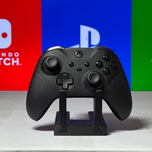 May include: A black Xbox controller on a stand in front of a red, blue, and green background with the logos for Nintendo Switch, Playstation, and Xbox.