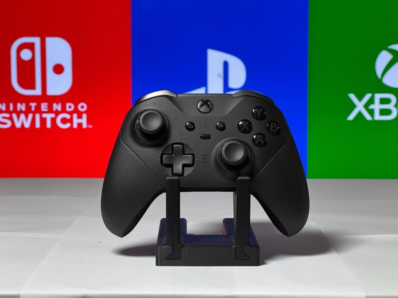 May include: A black Xbox controller on a stand in front of a red, blue, and green background with the logos for Nintendo Switch, Playstation, and Xbox.