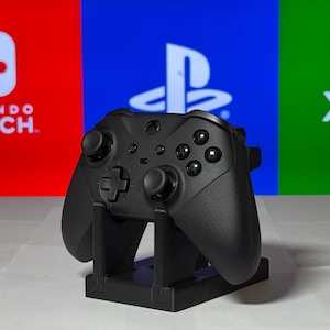May include: A black Xbox controller on a stand in front of a red, blue, and green background with the logos for Nintendo Switch, Playstation, and Xbox.