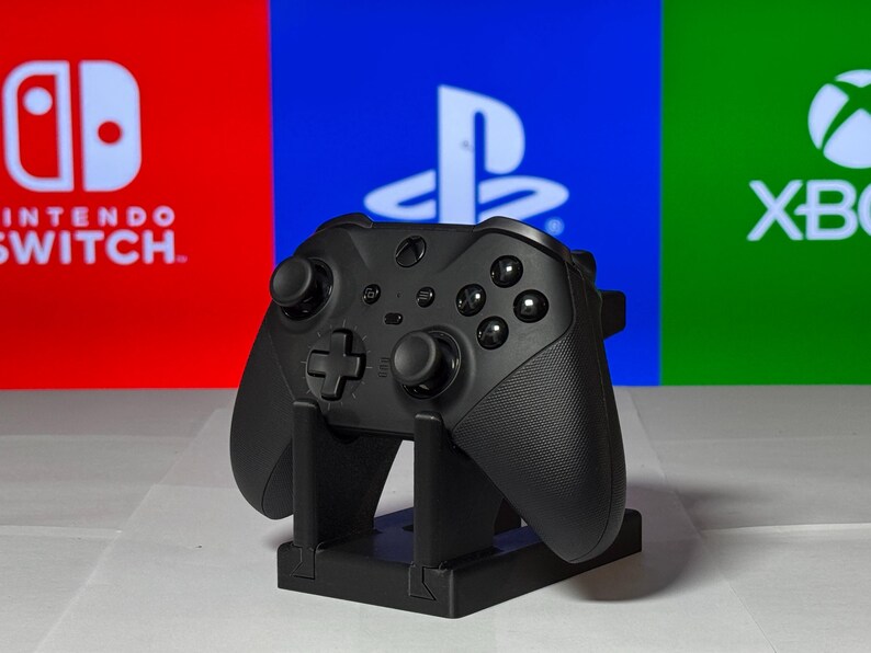 May include: A black Xbox controller on a stand in front of a red, blue, and green background with the logos for Nintendo Switch, Playstation, and Xbox.