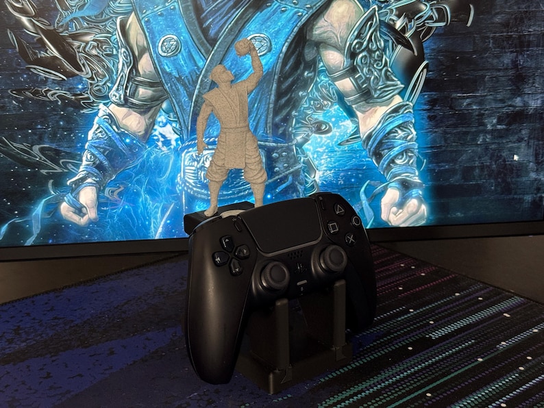 Może przedstawiać: Czarny kontroler PlayStation 5 spoczywający na czarnym stojaku, z małą figurką postaci z gry wideo na g&oacute;rze. Tło przedstawia niebiesko-biały obraz sztuki cyfrowej.