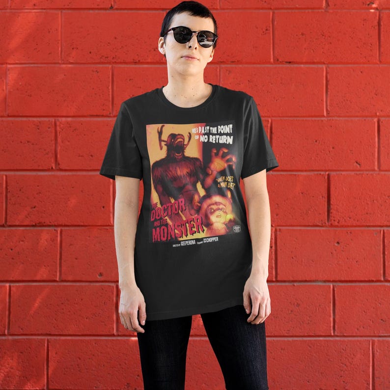 May include: Black t-shirt featuring a vintage movie poster design for "Doctor and the Monster." The poster art includes a monster illustration and the text "Past the Point of No Return." The shirt is worn by a person.