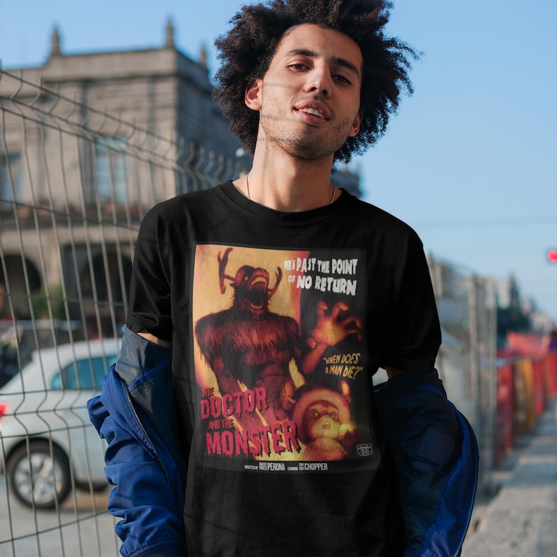 May include: Black t-shirt featuring a vintage movie poster design. The poster art depicts a monster with the text "THE DOCTOR AND THE MONSTER" and "PAST THE POINT OF NO RETURN". The shirt has a classic crew neck.