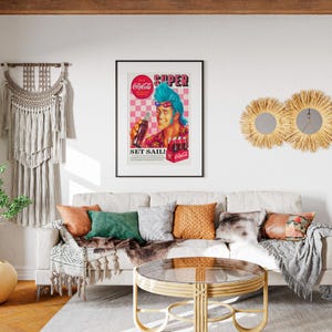 May include: A living room scene featuring a framed vintage Coca-Cola advertisement with the words "SUPER" and "SET SAIL!". The room includes a cream-colored sofa with decorative pillows, a round coffee table, and wall decor.