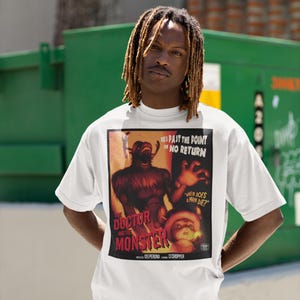 May include: White t-shirt featuring a vintage movie poster design for "The Doctor and the Monster." The poster art includes a monster illustration and the text "When Does a Man Die?" The shirt is worn by a person.