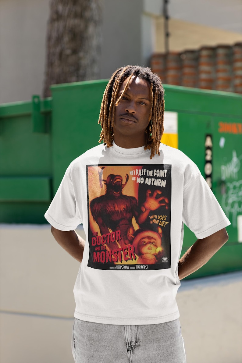 May include: White t-shirt featuring a vintage movie poster design for "The Doctor and the Monster." The poster art includes a monster illustration and the text "When Does a Man Die?" The shirt is worn by a person.