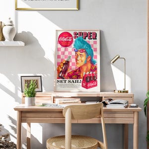 May include: A framed vintage advertisement for Cally-Cola, featuring a cartoon man with blue hair and sunglasses holding a bottle. The poster has a pink and white checkered background and the text "SUPER" and "SET SAIL!"