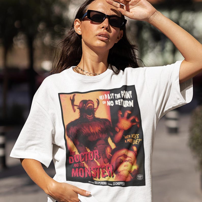 May include: White t-shirt featuring a vintage movie poster design. The poster has a red and orange background with a monster illustration and the text "THE DOCTOR AND THE MONSTER". Additional text includes "HES PAST THE POINT OF NO RETURN" and "WHEN DOES A MAN DIE?"