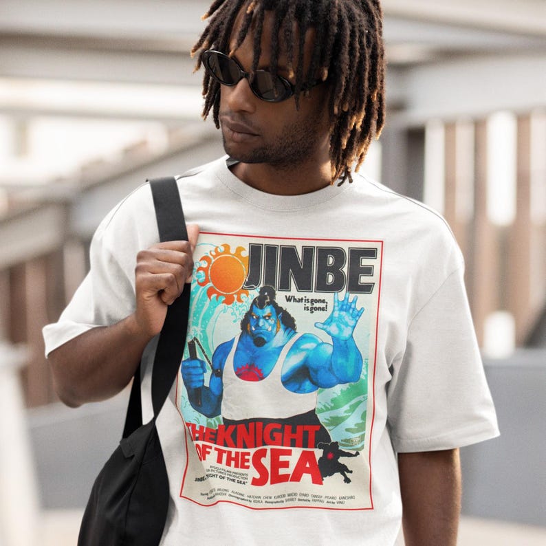 May include: White t-shirt featuring a colorful graphic of a blue character with the text "JINBE" and "THE KNIGHT OF THE SEA". The graphic includes a sun, waves, and the phrase "What is gone, is gone!"