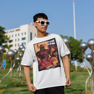 May include: White t-shirt featuring a vintage movie poster design for "Doctor and the Monster." The poster art includes a monster illustration and text. The shirt is worn outdoors on a sunny day.