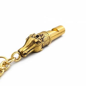 May include: A gold-colored whistle with a detailed horse head design. The whistle is attached to a gold chain. The horse head is intricately sculpted, and the whistle has a classic design.