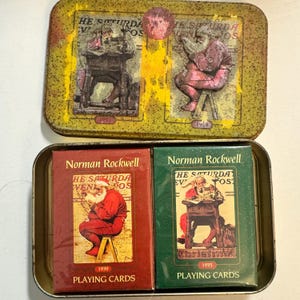 May include: Vintage Norman Rockwell playing cards in a metal tin. The tin features illustrations of Santa Claus, with two decks of cards inside, one red and one green. The cards are from 1939 and 1935.