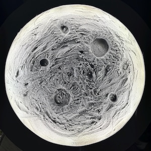 May include: A close-up of a grey and white textured sphere with multiple craters. The sphere is lit from the inside, creating a soft glow.