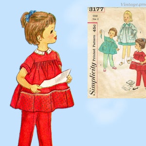 Può includere: Modello di cucito vintage Simplicity 3177 per un vestito e pantaloni per bambini. Il modello è per la taglia 2 ed è stampato su uno sfondo bianco con un bordo blu. Il modello mostra una bambina che indossa un vestito rosso con pois bianchi e pantaloni rossi.