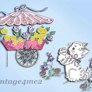 May include: A white kitten with a purple bow sits in a field of flowers. A pink flower cart with a yellow and white floral arrangement is in the background. The cart has a pink umbrella with white stripes.