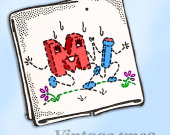 May include: A white card with a red letter M with a smiling face and blue stick figure with a smiling face. Both figures have black stitching around them and are on a white background with green and purple flowers.