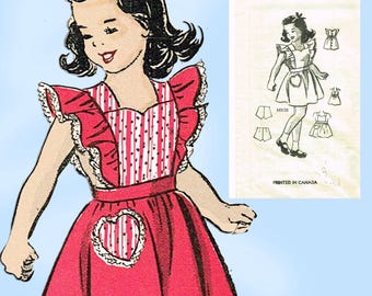 Op de afbeelding: Illustratie van een vintage rode schort met witte stippen en strepen, met een hartvormig zakje. De schort heeft ruches en maakt deel uit van een naaipatroon. De afbeelding bevat een tekening van een meisje dat de schort draagt.