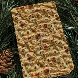 Peut inclure: Une pile de matzah, un pain sans levain traditionnel, enveloppée de ficelle brune et placée sur un lit d'aiguilles de pin vertes. La matzah est attachée avec une ficelle brune et a un aspect rustique et fait maison.