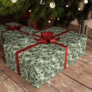 Op de afbeelding: Twee ingepakte cadeaus met een groen en bruin patroonpapier en rode strikken. De cadeaus liggen op een houten oppervlak.