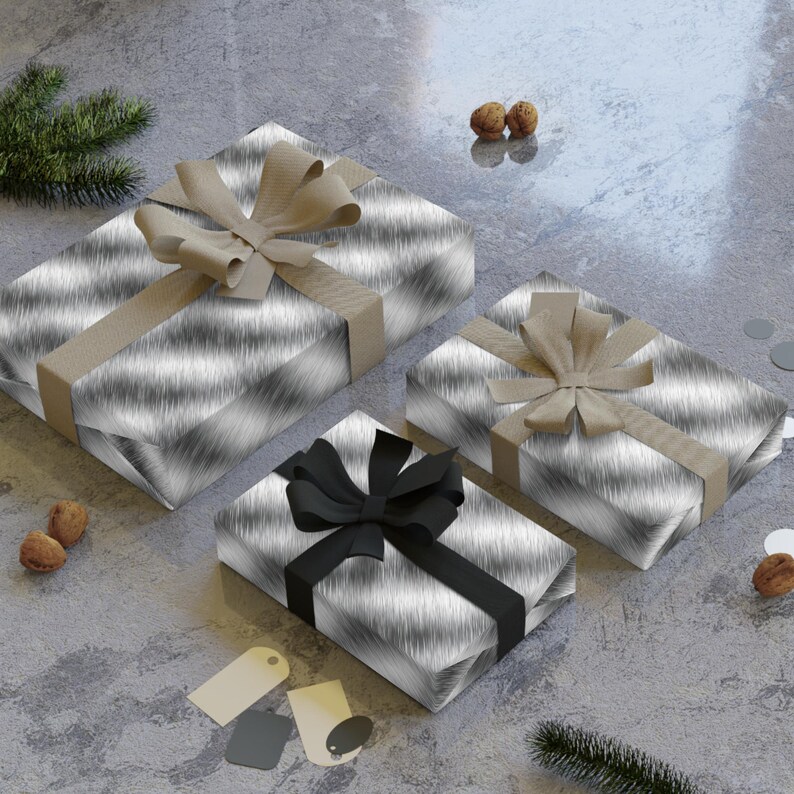 May include: Three gift boxes wrapped in a silver and black patterned paper. The boxes are tied with different colored ribbons. The largest box is tied with a brown ribbon, the medium box is tied with a brown ribbon, and the smallest box is tied with a black ribbon.