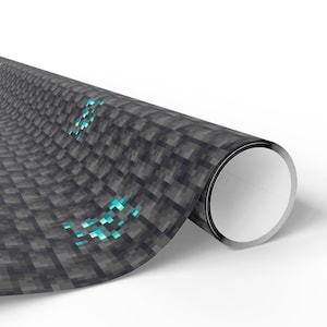 May include: Rolled-up roll of wrapping paper featuring a pixelated design of gray stone blocks with glowing blue gems. The paper has a white interior and is set against a white background.