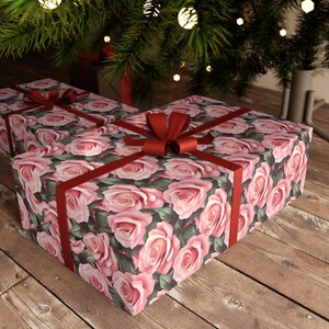 May include: Two gift boxes wrapped in pink rose patterned paper with red satin ribbon bows. The boxes are sitting on a wooden surface.