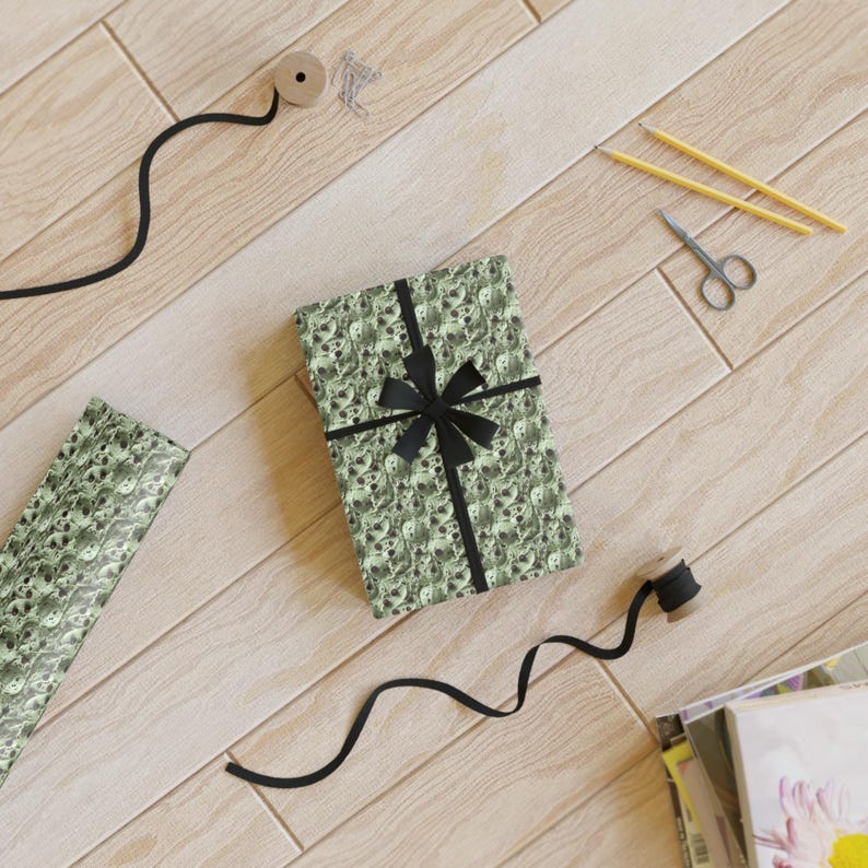 Op de afbeelding: Een groene en zwarte cadeaupapier met een schedelpatroon. Het cadeaupapier is om een ​​doos gewikkeld met een zwart lint en strik. De doos staat op een houten oppervlak.