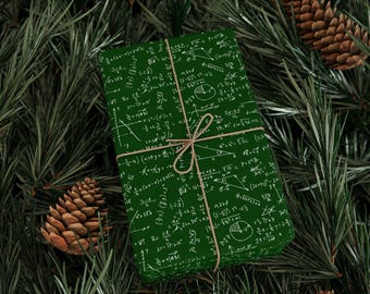 May include: A green gift box wrapped in paper with white mathematical equations and formulas. The box is tied with twine and is sitting on a bed of green pine needles.