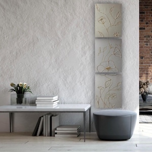 Puede incluir: Un conjunto de tres paneles de arte mural vertical con un diseño floral en relieve y texturizado en tonos crema y oro. La obra muestra tallos, hojas y flores delicadas con un acabado táctil y tridimensional sobre un fondo neutro.
