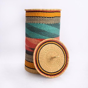 May include: A tall, cylindrical woven basket with a matching lid. The basket features horizontal stripes in teal, orange, red, black, and yellow. The lid is round with a central knob and a decorative border.