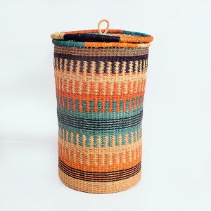 May include: A tall, cylindrical woven basket with a lid. The basket features horizontal bands of orange, teal, black, and natural beige. The lid has a small loop handle. The basket is likely used for storage or laundry.